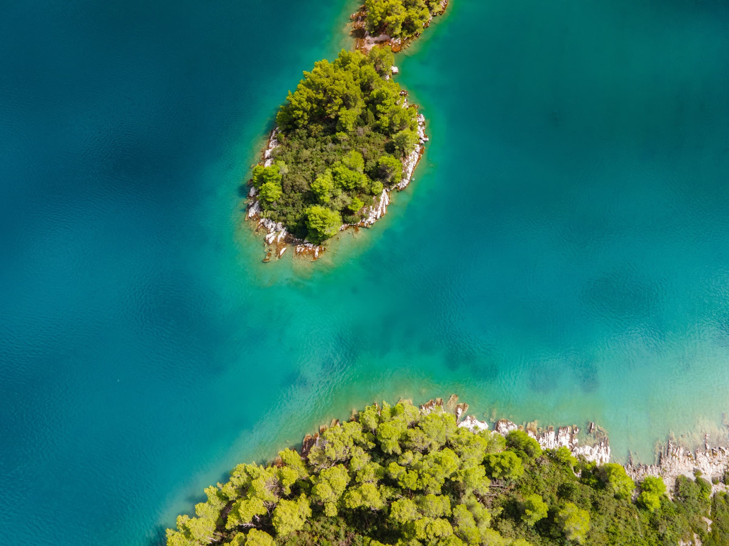 Aerial view of two small forested islands in the turquoise waters of the Croatian Adriatic.
