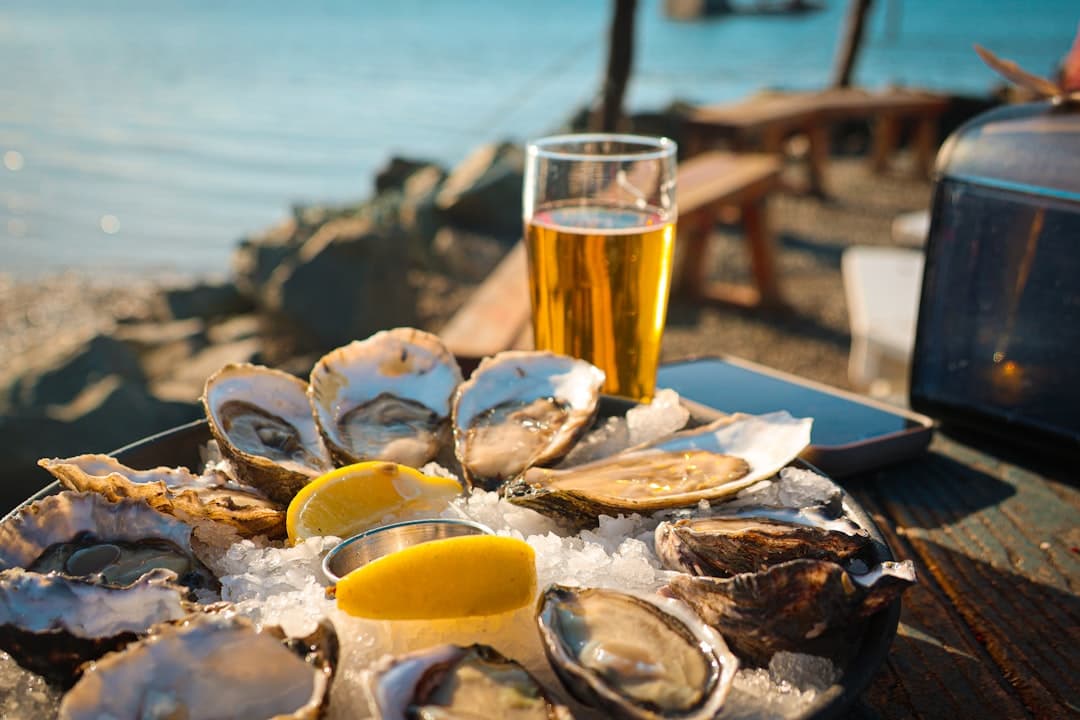 Fresh European flat oysters opened on ice with lemon wedges, served beside the water.