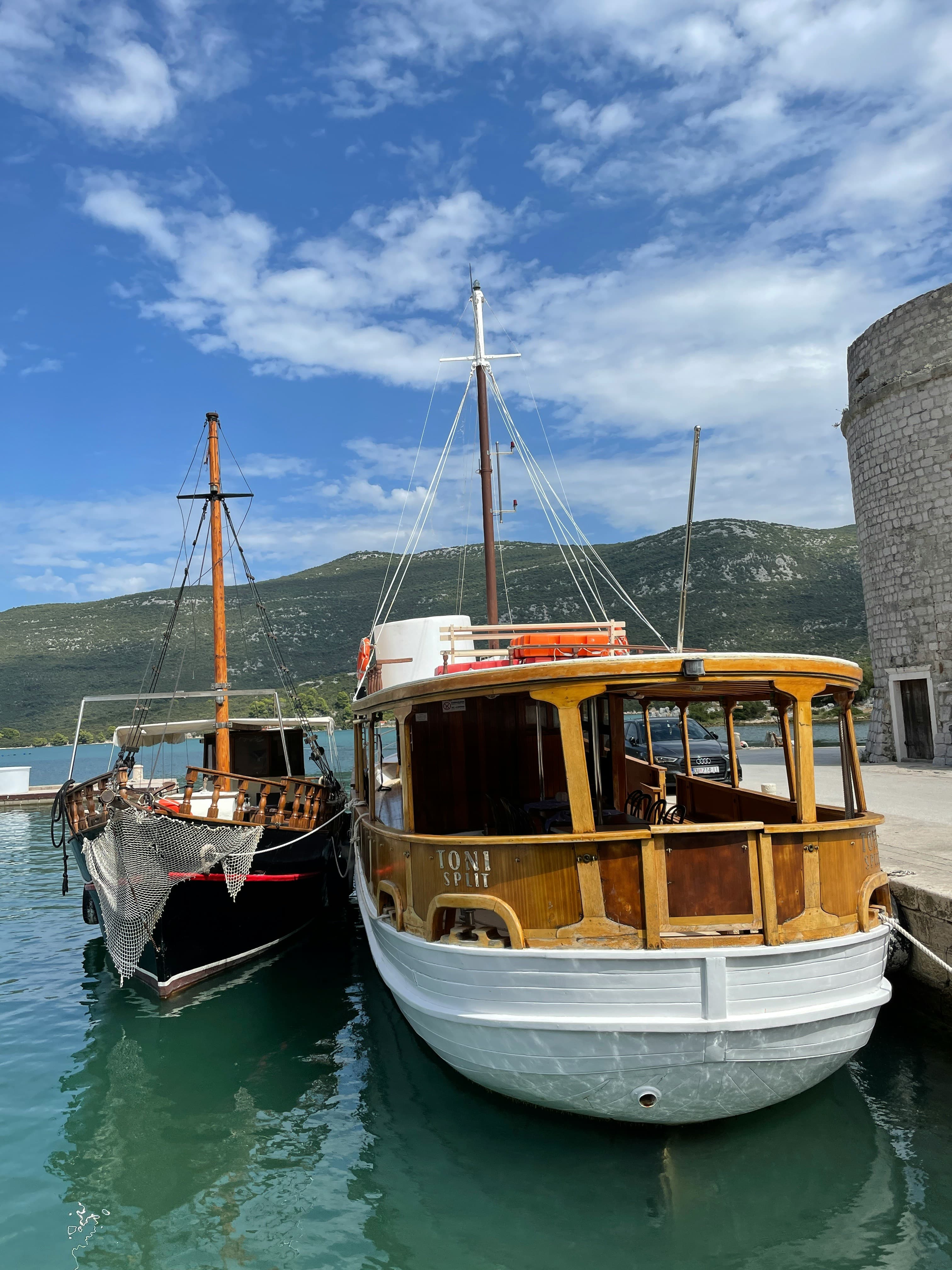 Two wooden boats moored at Mali Ston harbour with a round stone tower of the Ston walls visible on the right.
